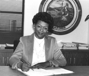 Woman sitting at desk with California seal in the background.