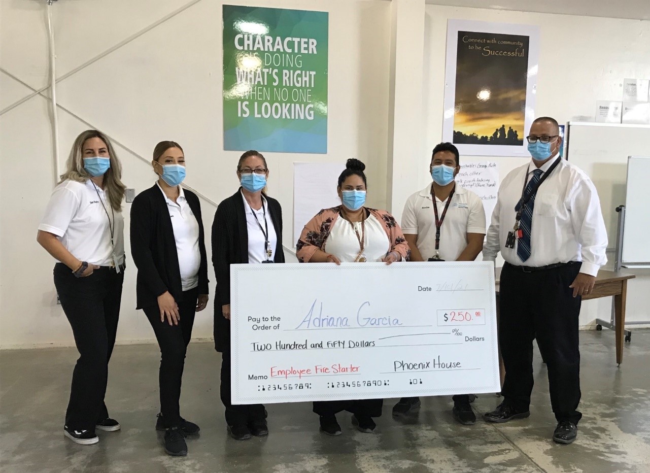 Six people wearing masks hold an over-sized check made out for $250 to Adriana Garcia from the Phoenix House.