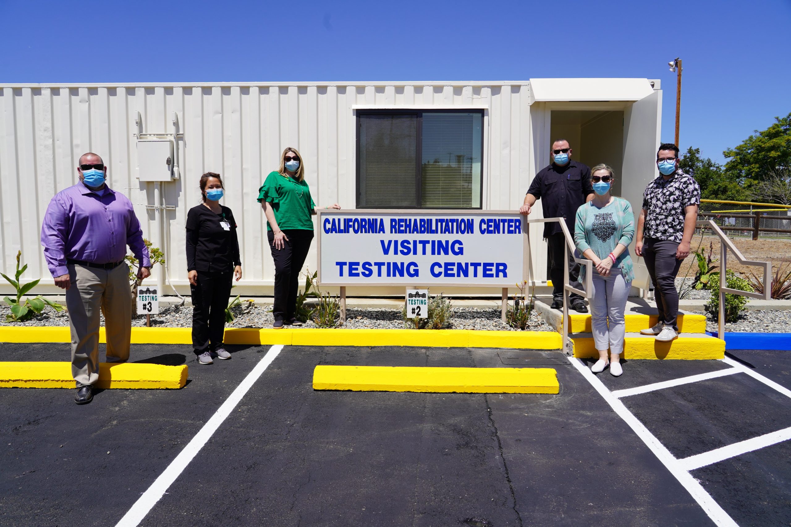 Staff stand at a sign that says California Rehabilitation Center Visitor Testing Center.