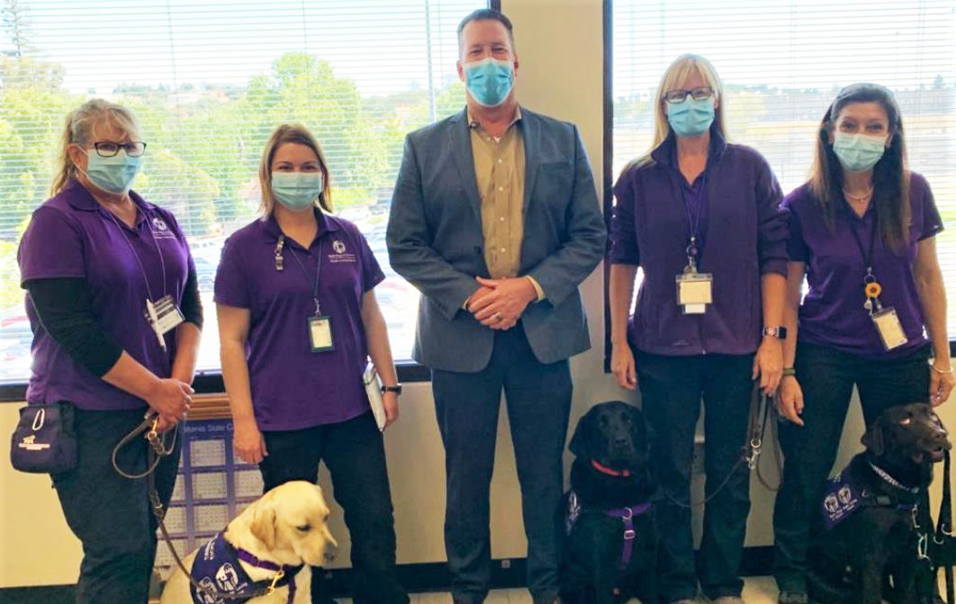 Service dogs with four women wearing purple and the Sacramento prison warden.