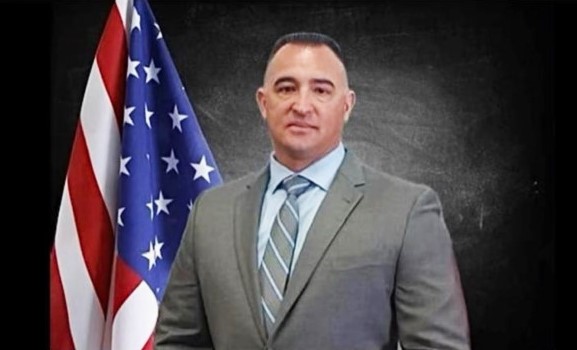 Agent Delgado in jacket and tie with a US flag.