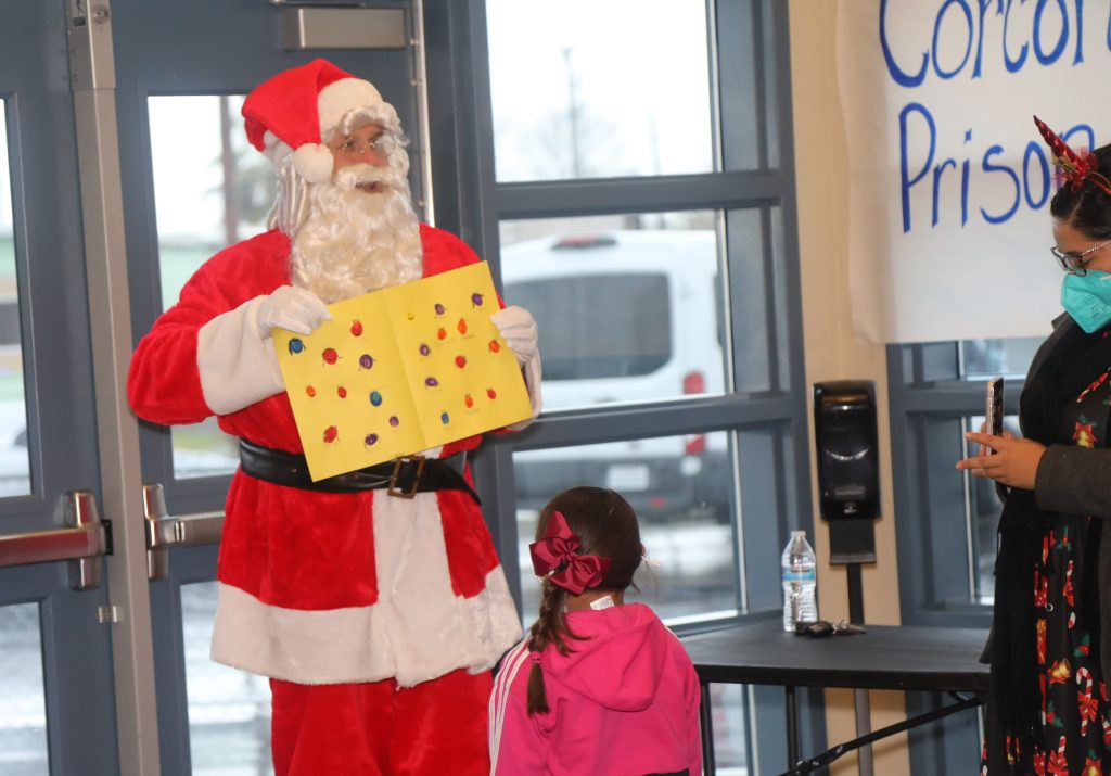 Santa stands in a school with a child and an adult.