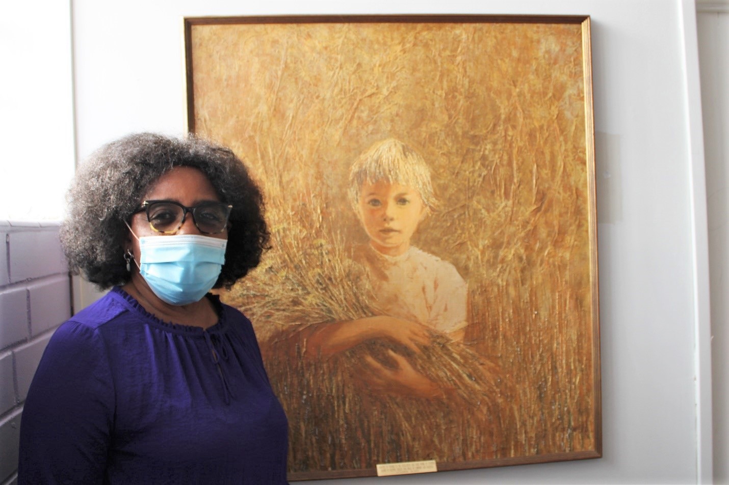 Cynthia Brown wears mask next to painting of a boy.