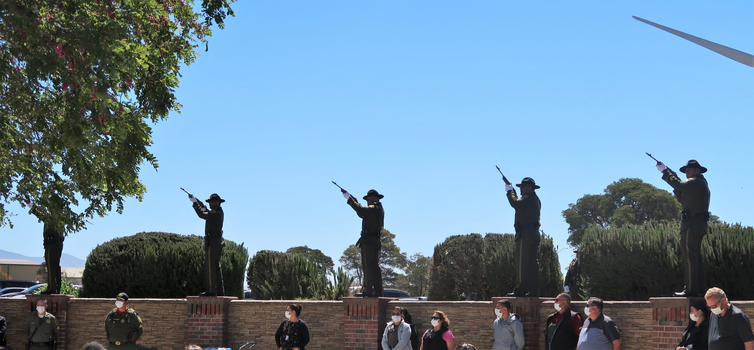 21 gun salute at CTF memorial with men on a wall and holding rifles.