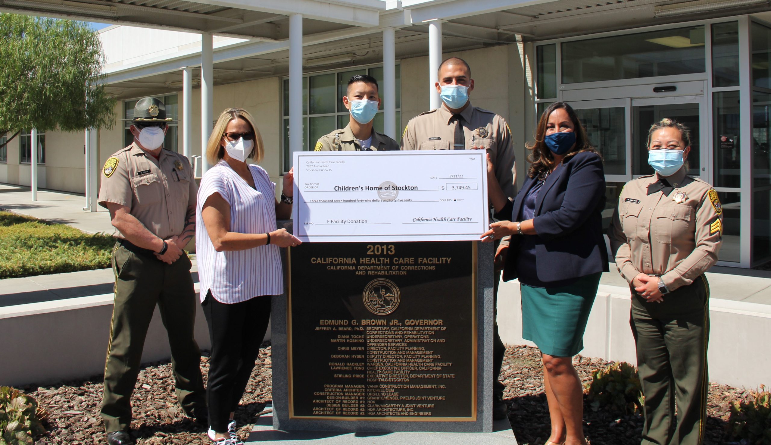 Correctional staff and people in regular clothing with an oversized check and the California Health Care Facility sign.