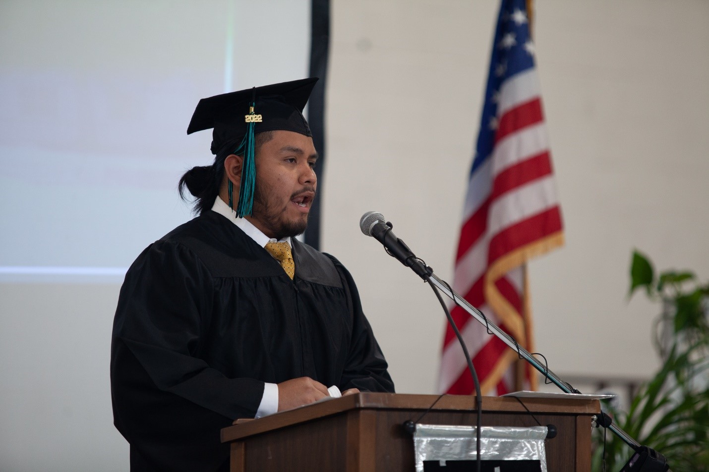 Man in cap and gown speaks at a lectern.