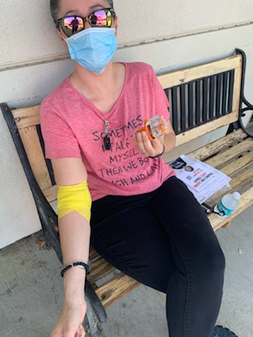Woman wearing pink shirt and showing off her yellow bandage after donating.