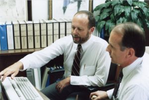 Data entry with parole office as two men look at a computer screen.