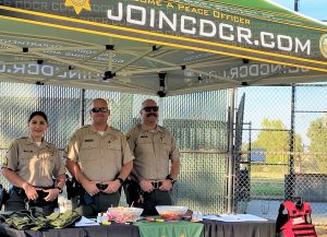 Three correctional sergeants stand under a pop-up tent. The front of the tent has the website JoinCDCR.com.