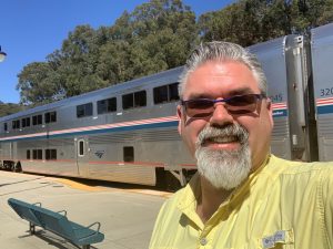 Teacher Craig Stewart wears sunglasses while standing beside a train.