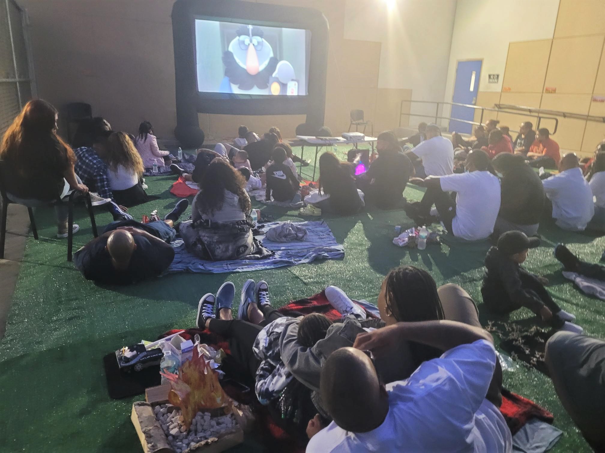 Children and their parents spread out on blankets with to watch a movie.