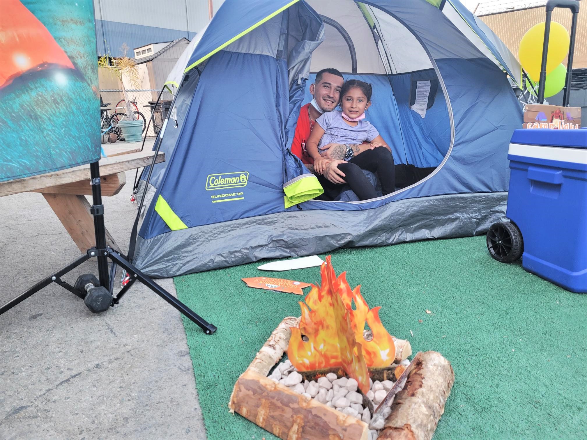 A father and child sit inside a tent while a fake campfire is out front.
