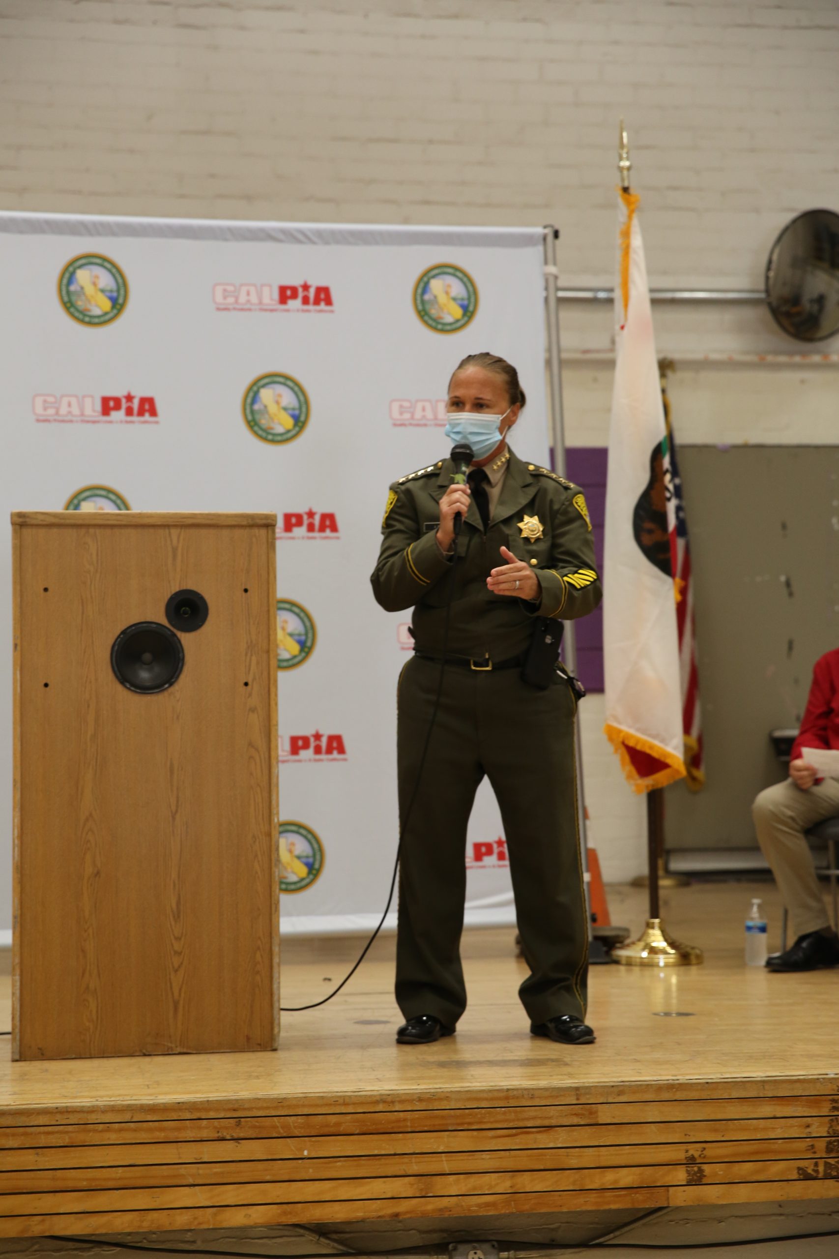 A woman in a correctional uniform and mask holding a microphone