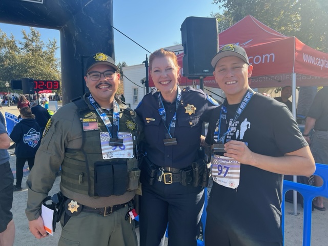 Officer Duenas in full uniform, a police chief in uniform and a man in an event shirt.