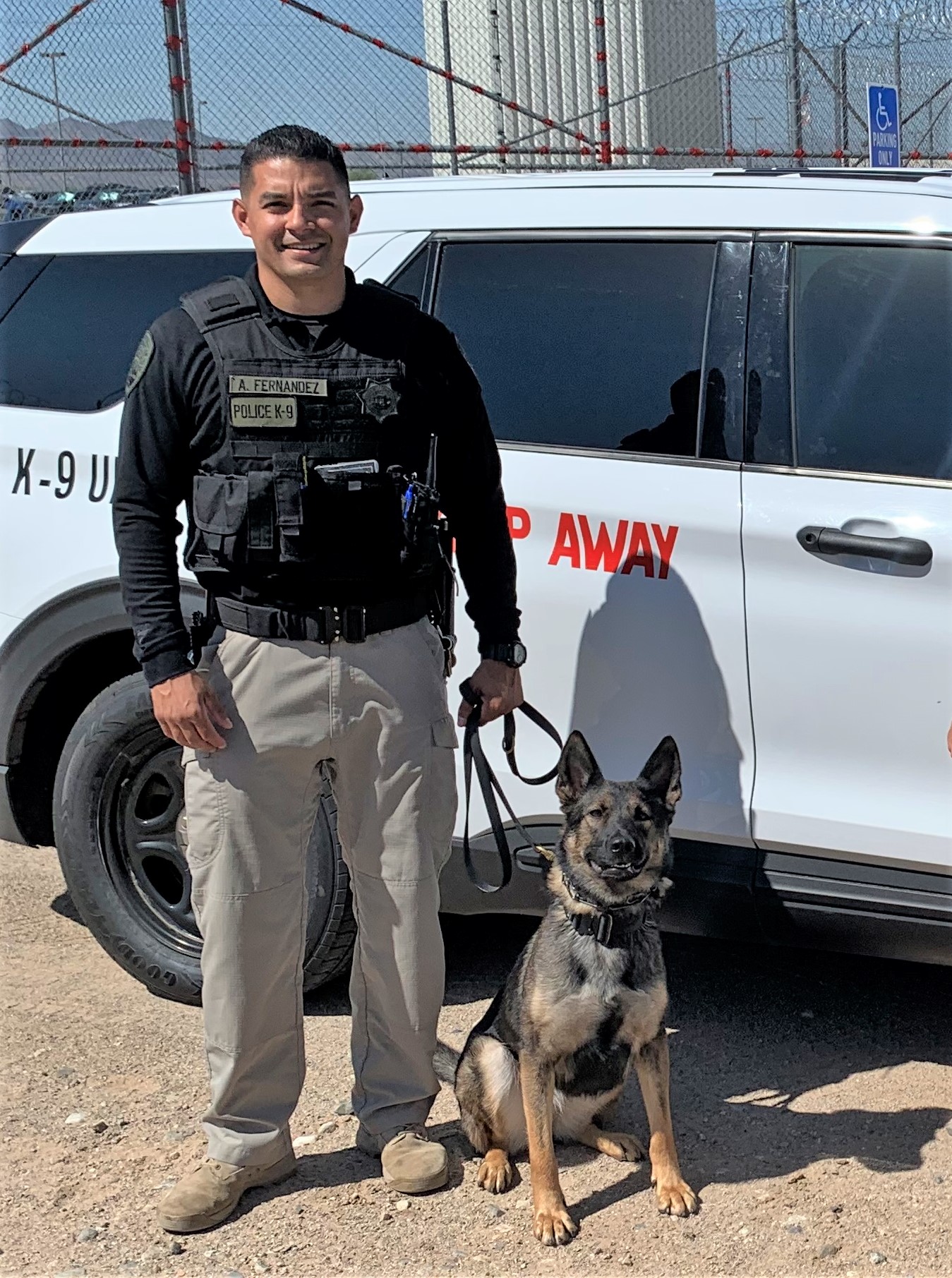 Correctional officer and his K-9 in front of a vehicle.