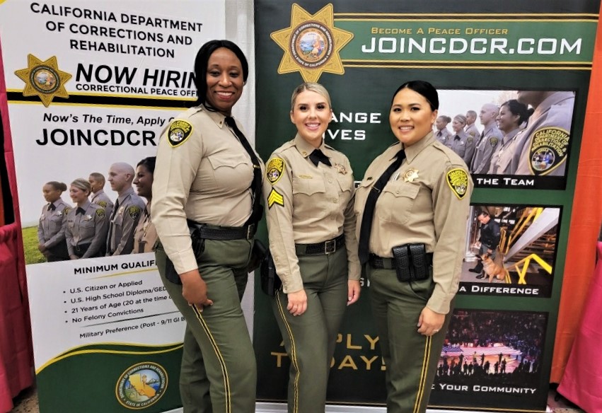 Three CCWF correctional staff in uniform at a CDCR recruitment booth along with GARE.