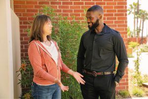 Woman speaking to man with brick wall behind them.