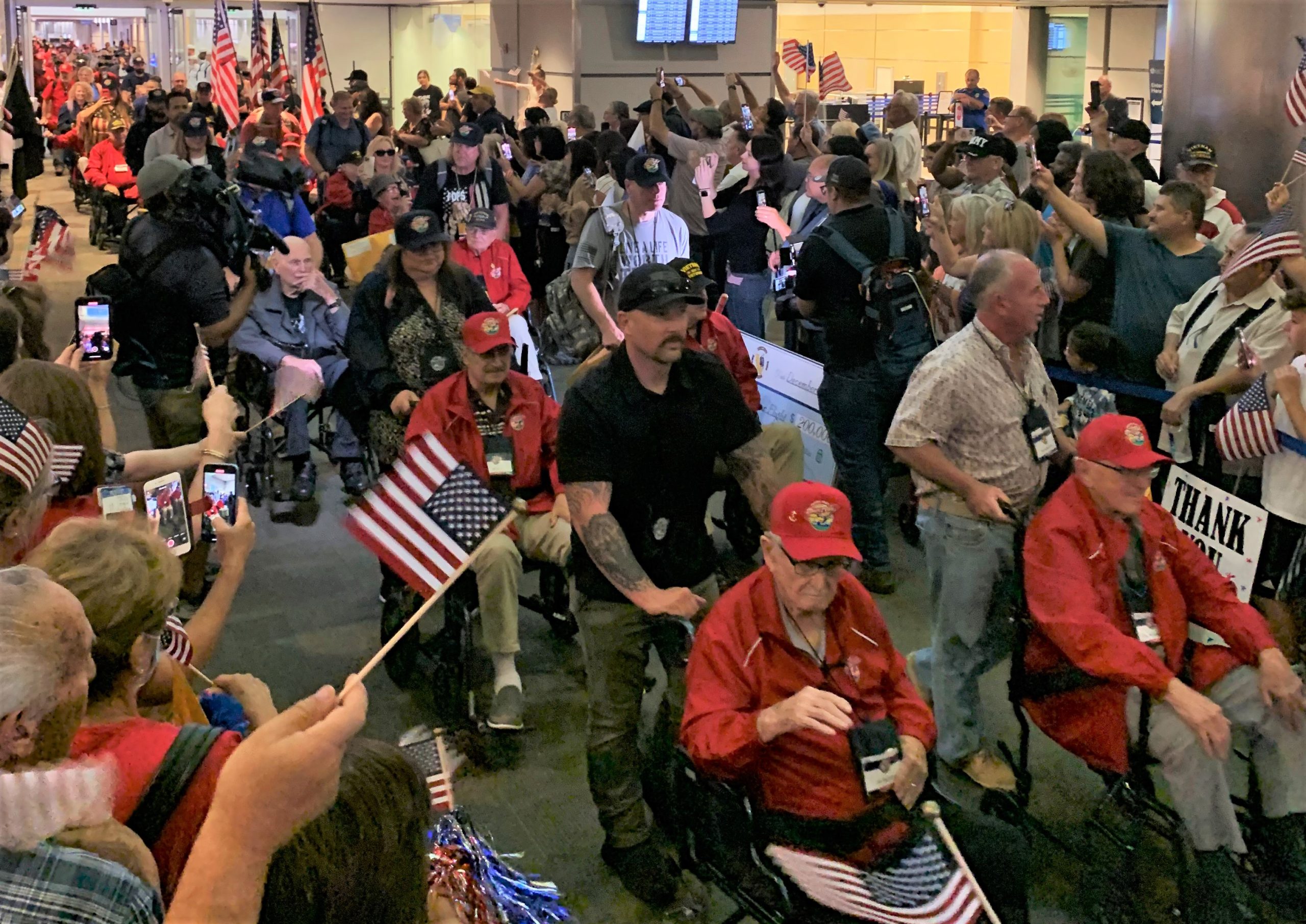 Veterans in wheelchairs are greeted by cheering crowd.