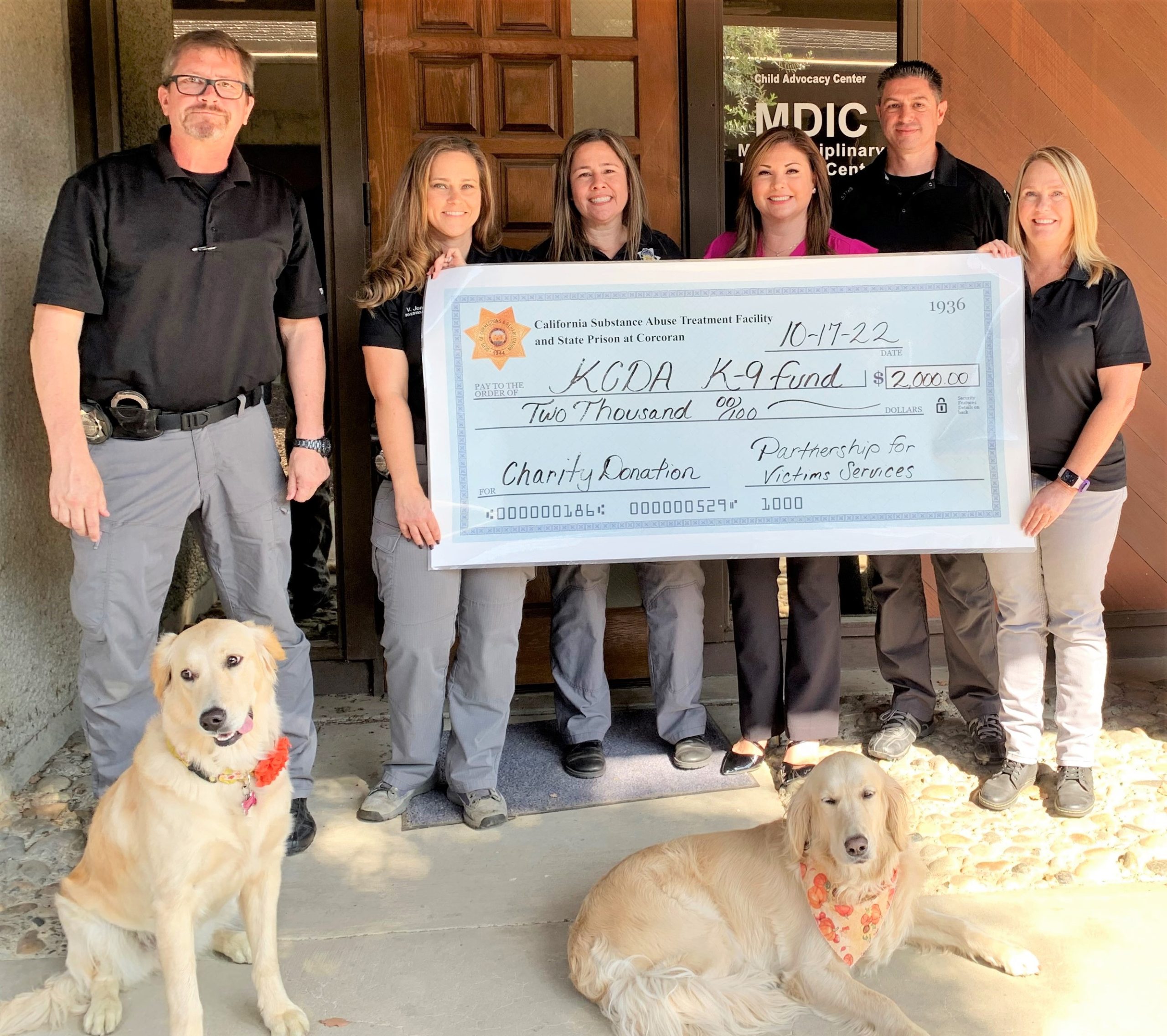 Dogs lie down in front of an oversized check presentation from SATF/SP staff to Kings County organizations.