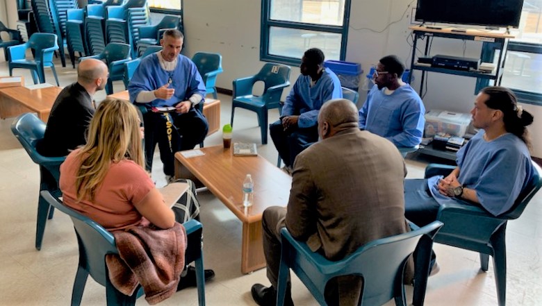 Incarcerated people and other sit around a small table.
