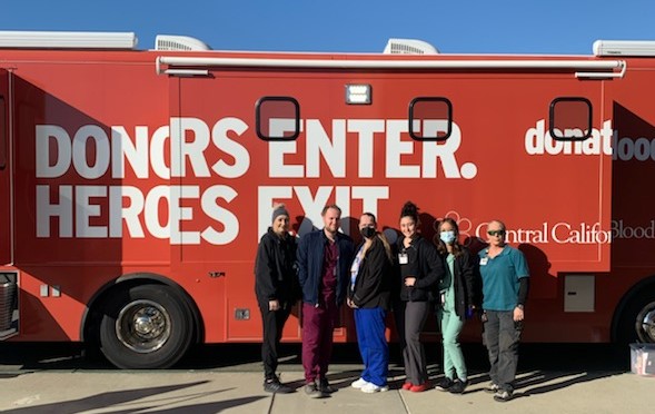 Prison staff stand in front of blood donation mobile unit with the words 'Donors Enter. Heroes Exit.'