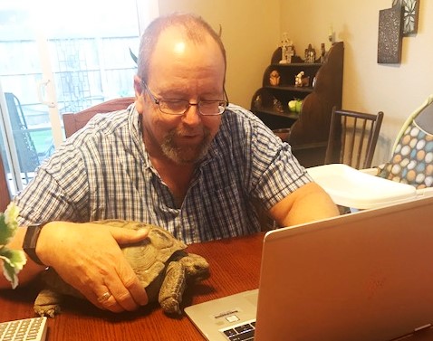 Man at a table with a laptop and turtle.