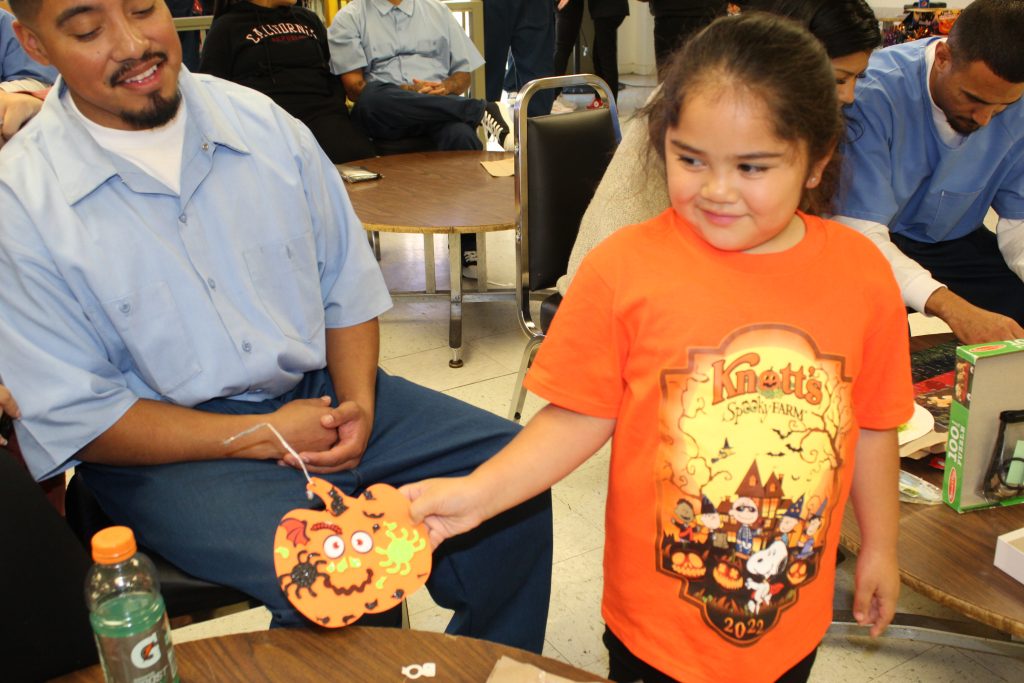 Child holds a decorated paper pumpkin.