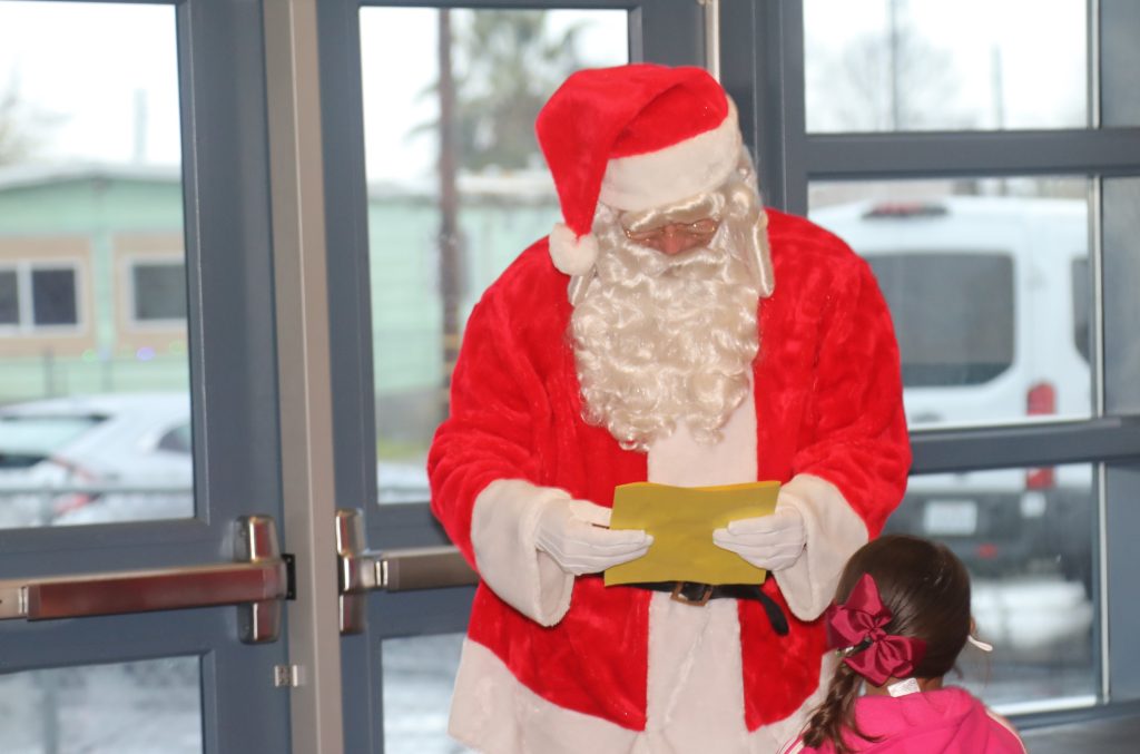 Man in Santa suit holds letter while child stands nearby.