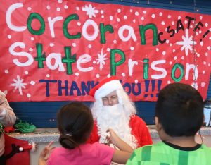 Volunteer Santa DJ Cunning at a school with thank you sign behind him addressed to prison staff.