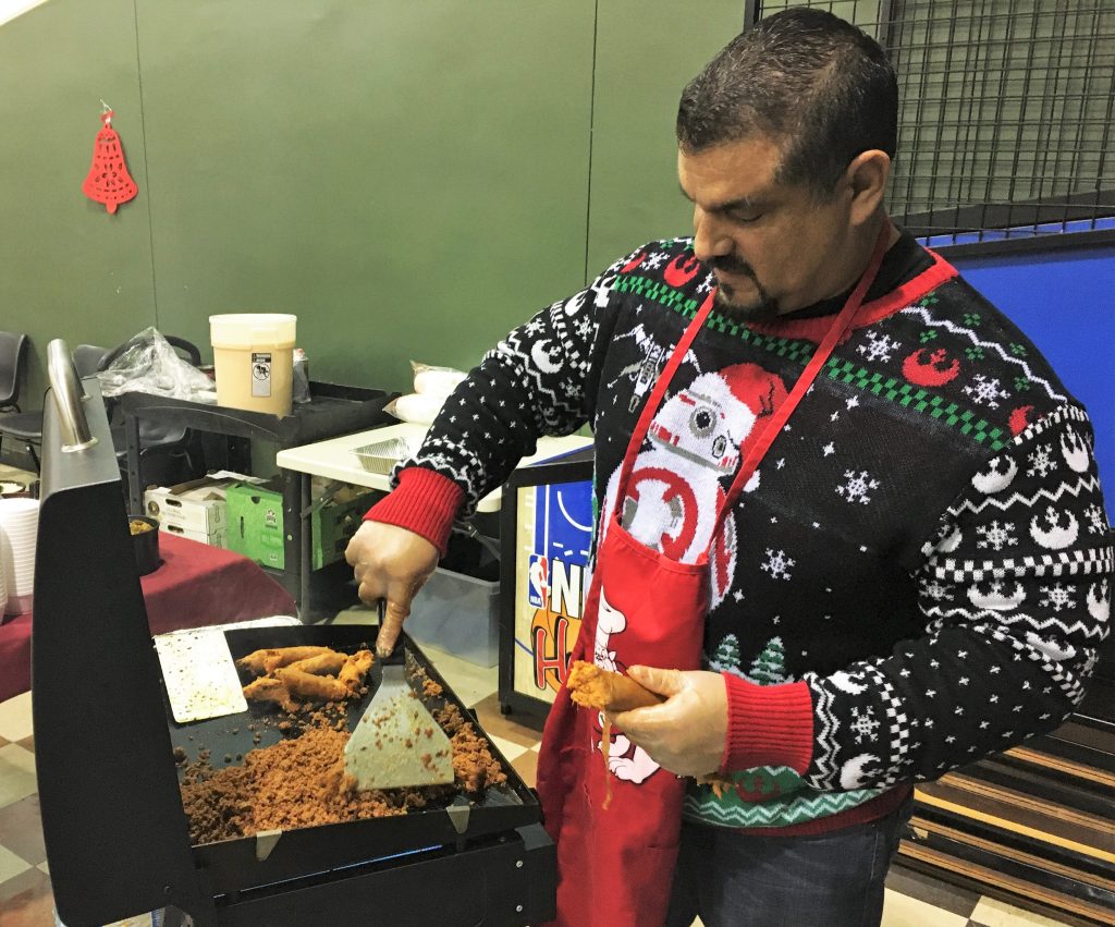 Man wearing holiday sweater cooks chorizo at a grill.