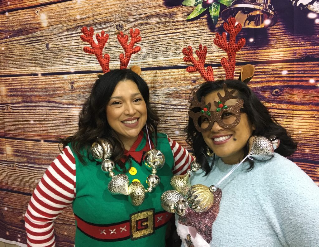 Two women wearing Christmas outfits in front of a photo backdrop.