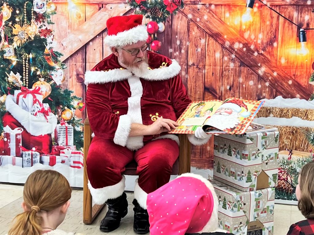 Santa reading a book to school children.