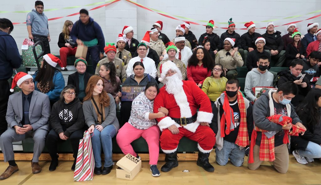 Young girl hugs Santa while prison staff and school students sit on bleachers. 