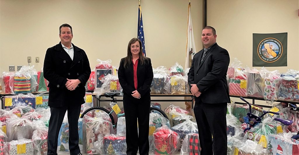 Three Sacramento prison leaders stand in front of a pile of gifts to help families in need during the holidays.