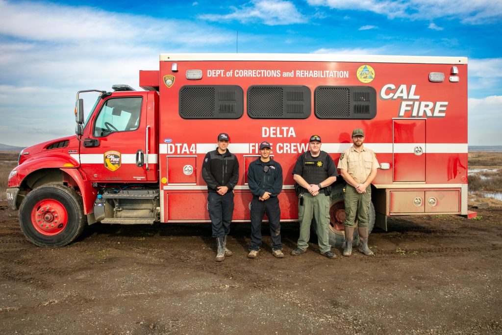 Four men in uniform stand by a CAL FIRE truck