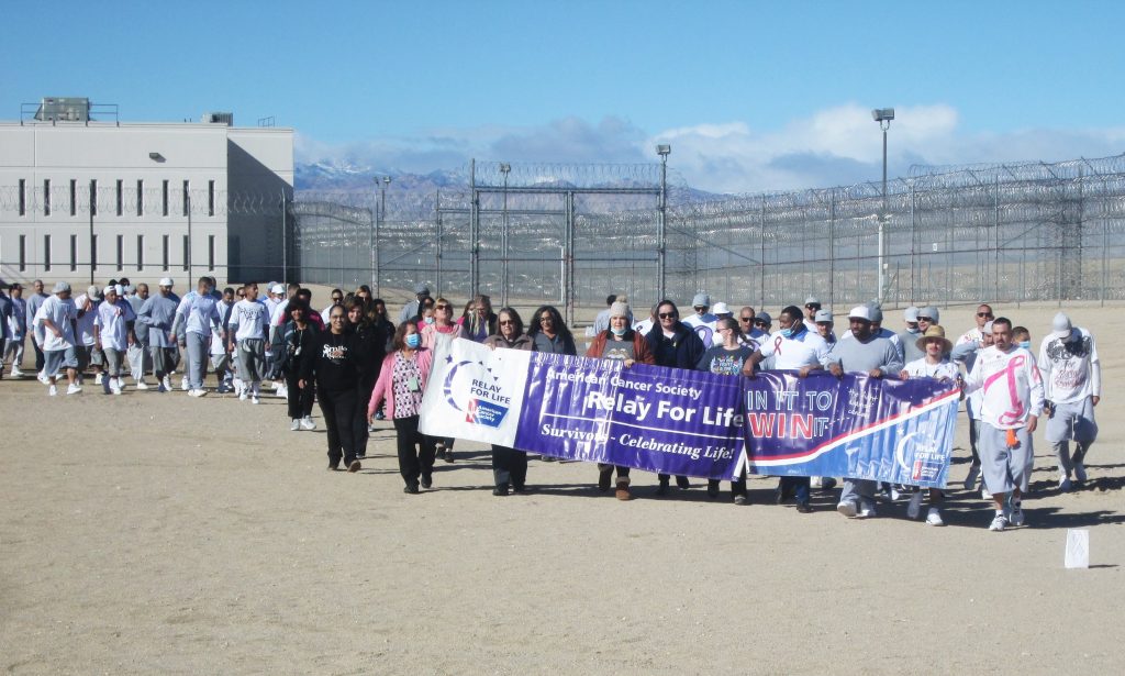 A prison yard with people walking while holding a Relay for Life banner.