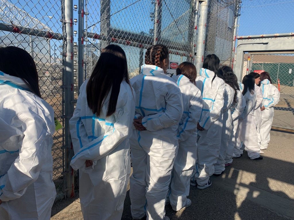 Youth in white jumpsuits stand in a prison sallyport