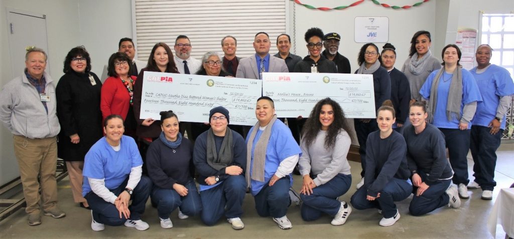 Incarcerated females and prison staff hold over-sized donation checks. 