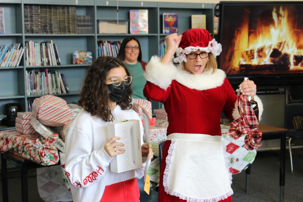 Mrs. Claus pumps her fist in the air while a student holds a new computer tablet.