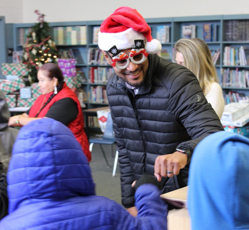 Mayor wearing a Santa hat and sunglasses fist bumps students at a Stockton school.