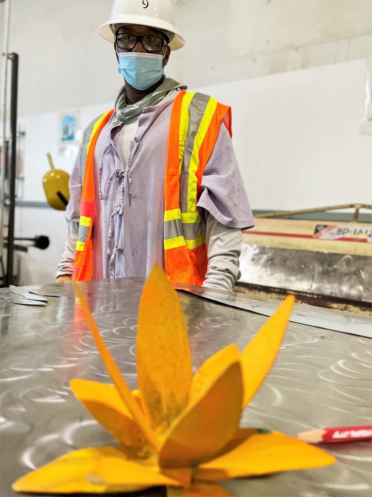 Student stands behind metal plant art.