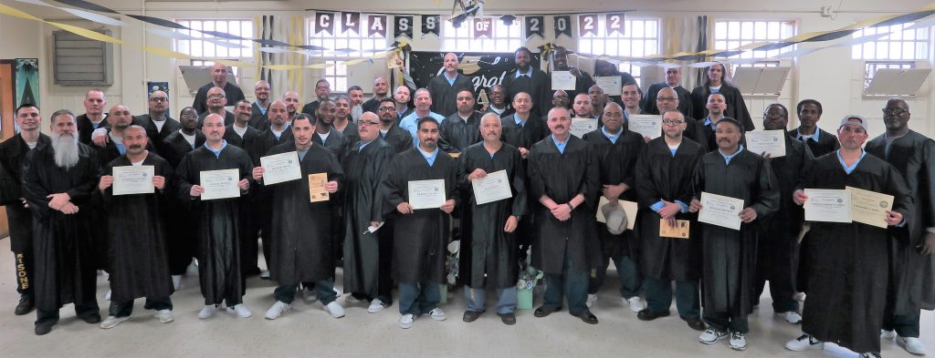 Education graduation ceremony for incarcerated people who are wearing caps and gowns while holding their certificates and diplomas.