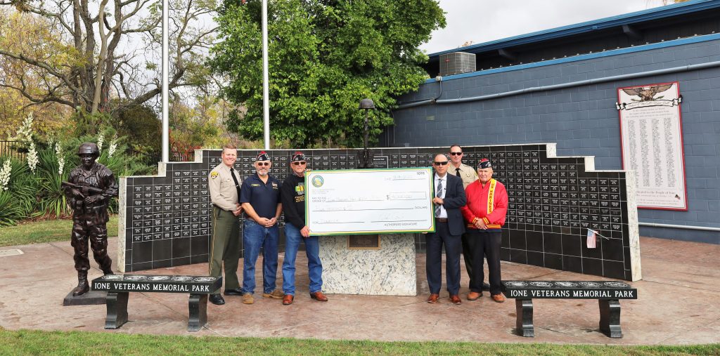 Veterans Memorial Park in Ione with prison staff and Veterans of Foreign Wars representatives with oversized donation check.