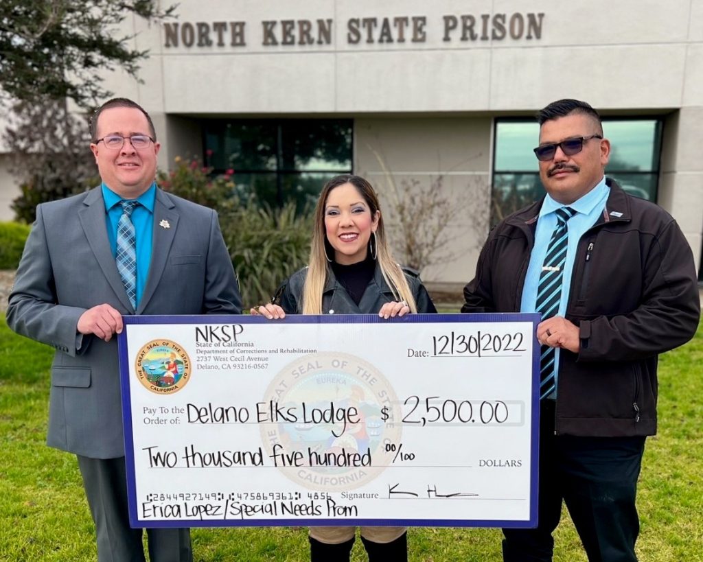 Two prison officials and a high school special education assistant with an over-sized check in front of North Kern State Prison.