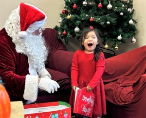 Santa and a smiling little girl beside a Christmas tree.