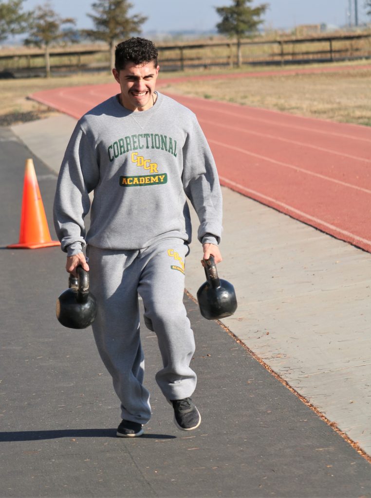 Correctional officer cadet carries weights around a track.