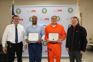 Two incarcerated people receive certificates from prison officials.