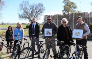 Pleasant Valley State Prison (PVSP) incarcerated artists and the bike program donated items to the Coalinga Chamber of Commerce for a silent auction. Community members and staff are shown with the items.