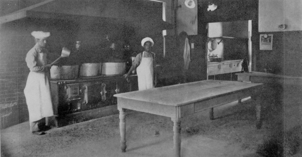 Youth offenders in a kitchen with vats, pots and a table.