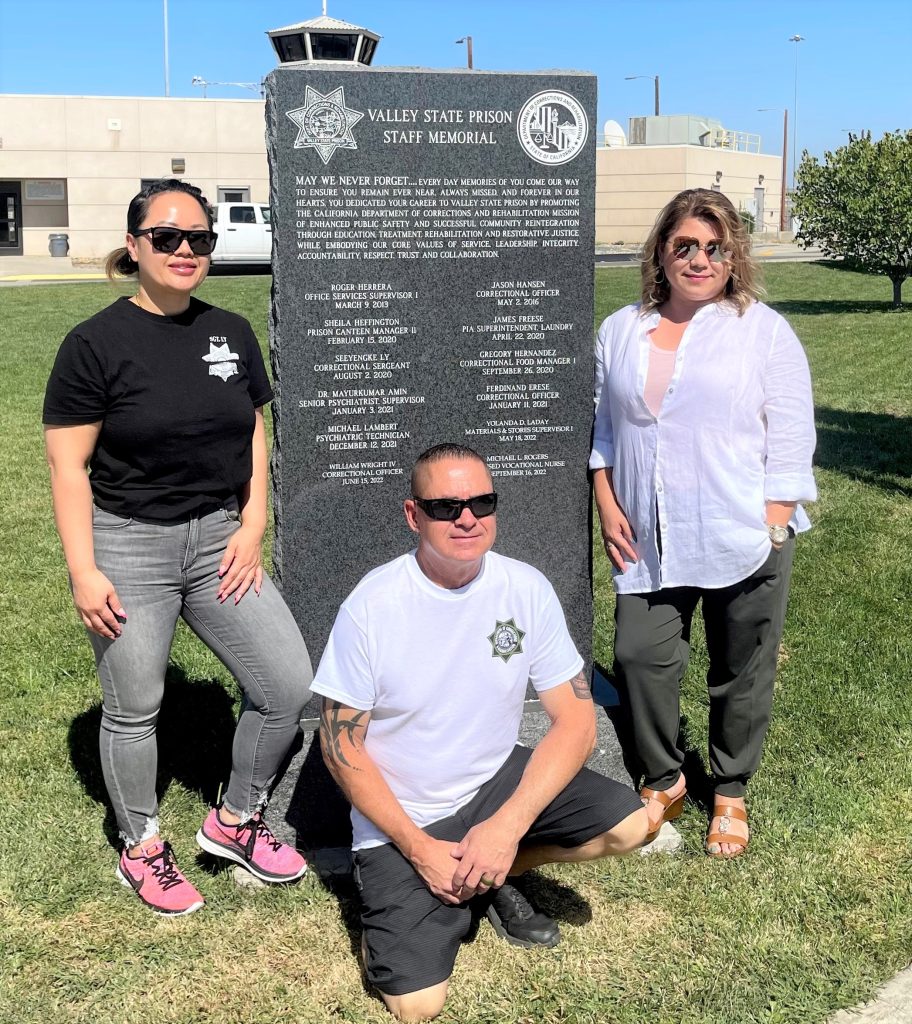 Valley State Prison memorial wall with names and three people standing beside it.